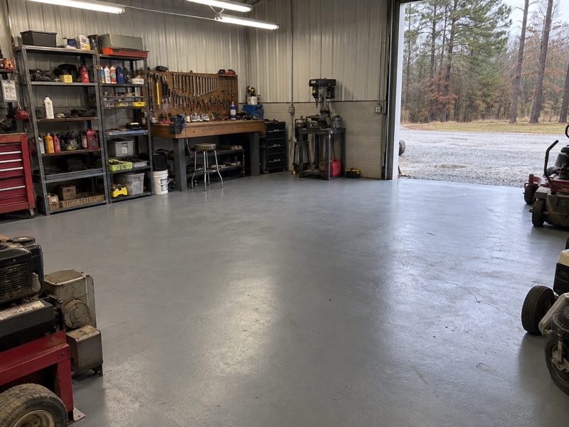 Gray coated floor in a metal-sided workshop with tool shelves and a workbench